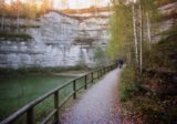 Jasne skały dawnego kamieniołomu nad niewielkim jeziorkiem i ścieżka z drewnianą barierką w Kielcach