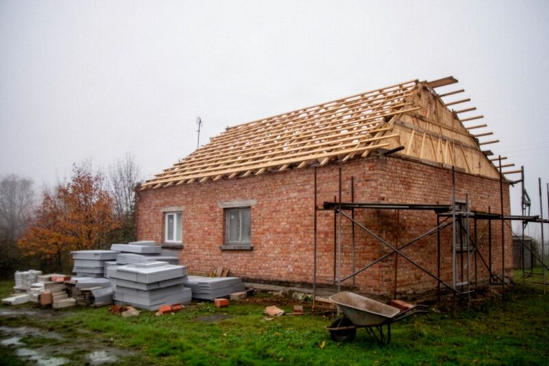 Stary ceglany dom w trakcie remontu z odsłoniętą więźbą dachową i rusztowaniem